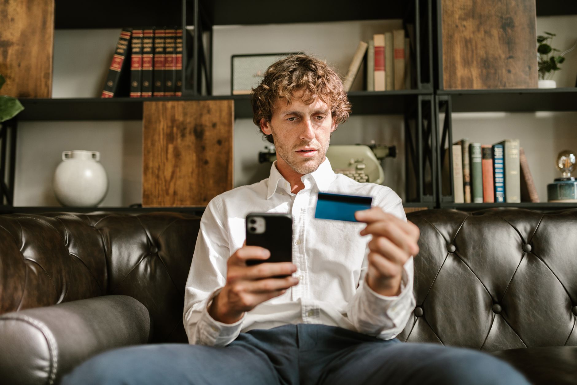 Person holding a credit card and looking at a phone with a worried expression.