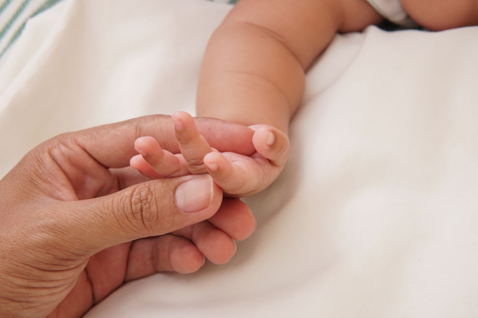 A close-up of a parent holding a newborn baby's hand, with no visible identifying hospital details.