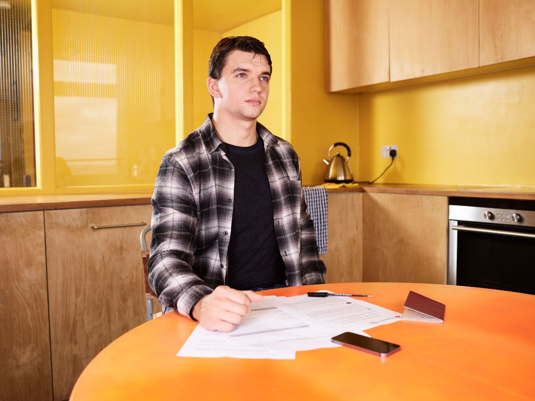 A person looking at a credit report on a smartphone at a kitchen table with paperwork nearby.