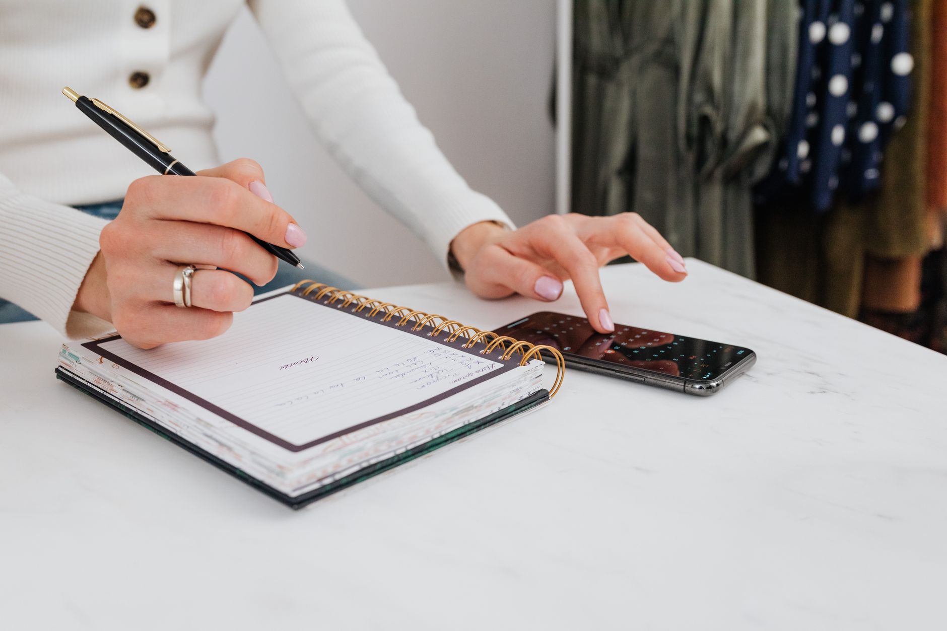 Person storing security freeze PINs in a notebook beside a smartphone on a desk.