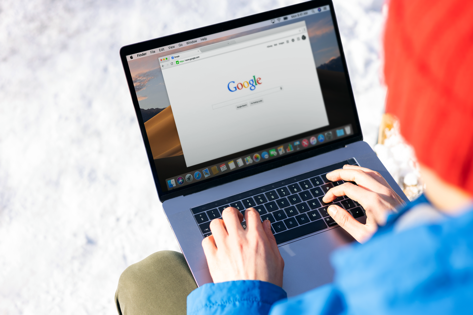 A person in a home office searching for their own name on a laptop while writing notes in a notebook.