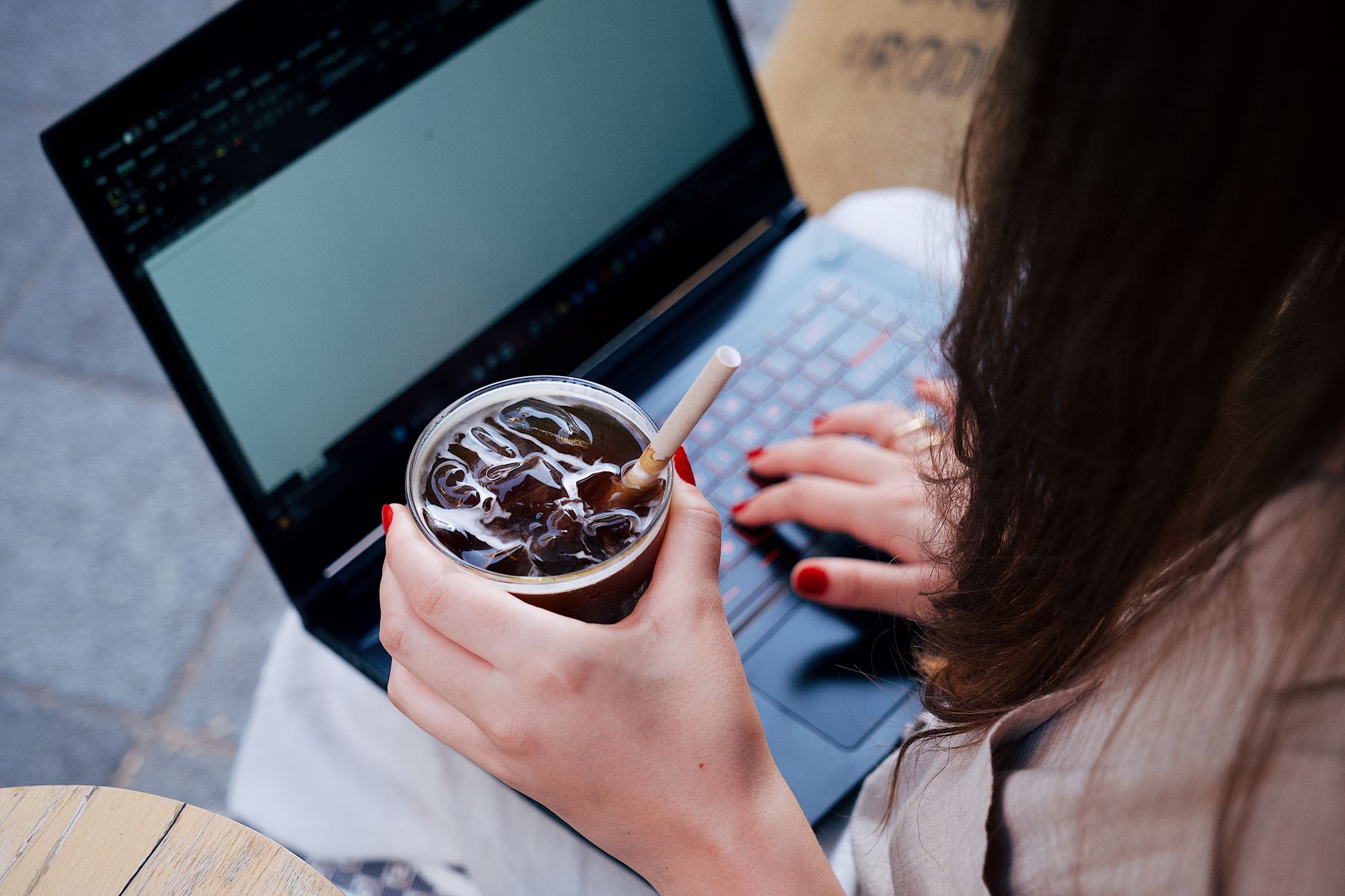 A woman using a laptop at a cafe table while another person sits nearby, illustrating a public workspace.
