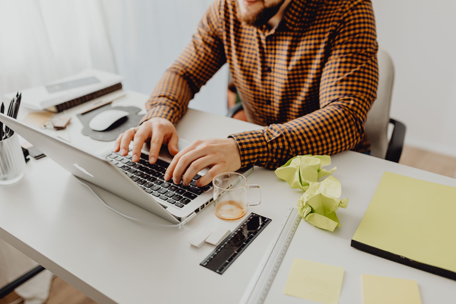 A person sits at a desk with a laptop and paper documents, looking at personal records.