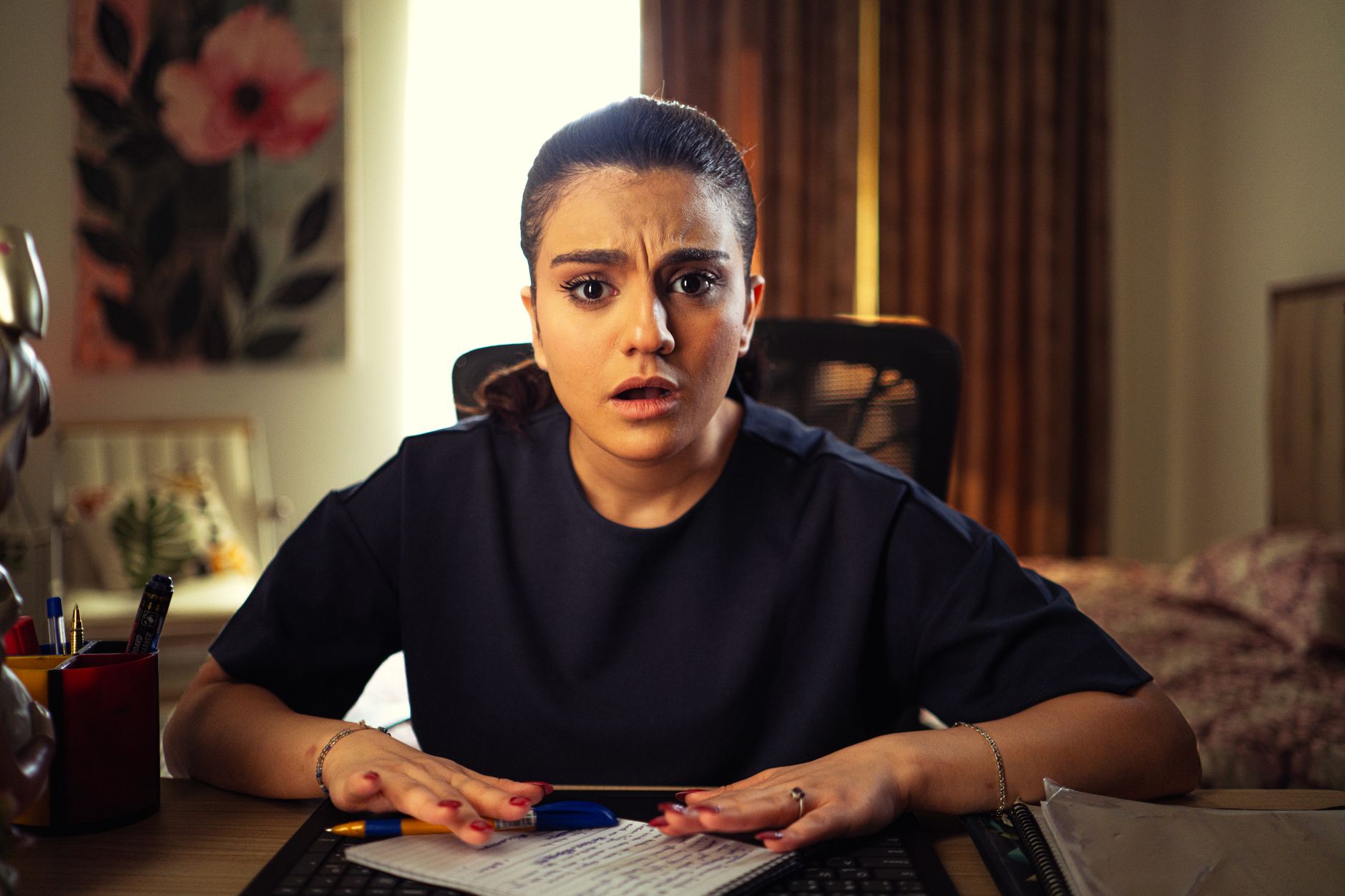 A person sits in a dimly lit room looking at a laptop with a worried expression.